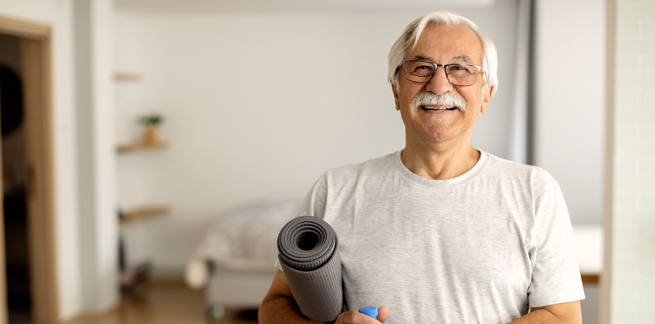 A man smiles while holding his exercise mat